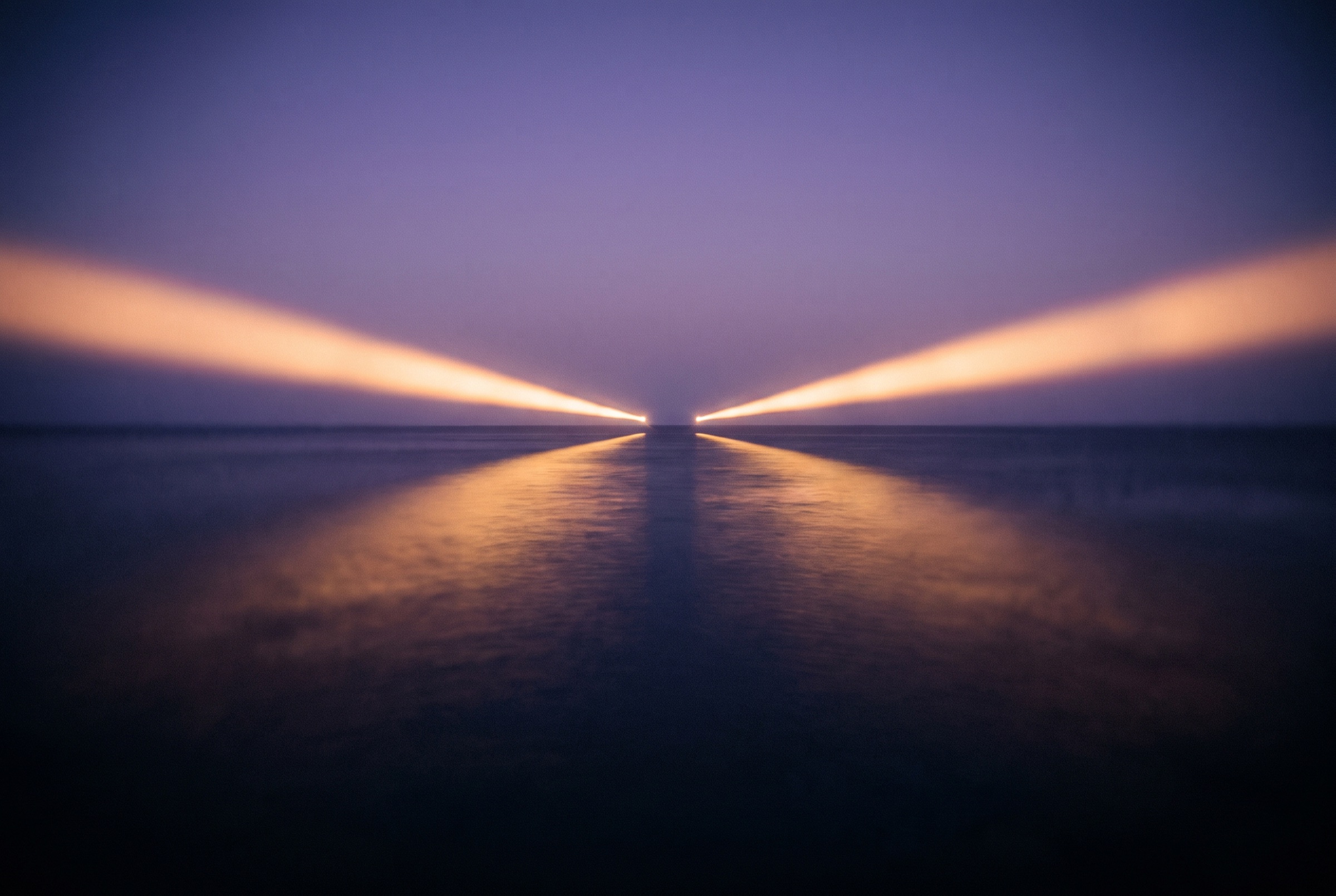 Two beams of warm light meeting over a dark ocean horizon